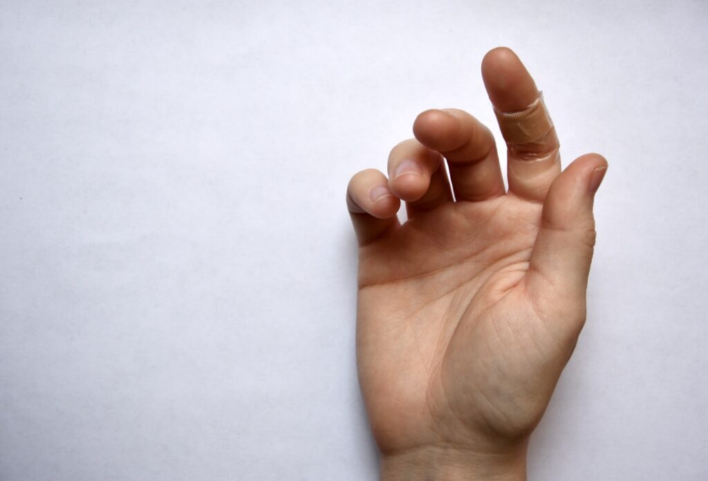 Photo of a hand having a wound covered by plaster on a finger on white background